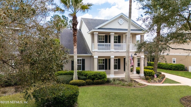 neoclassical / greek revival house featuring a balcony, stucco siding, covered porch, and a front yard