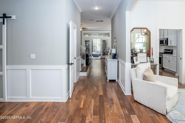 hallway with ornamental molding, a barn door, visible vents, and a healthy amount of sunlight