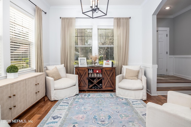 living area featuring arched walkways, wainscoting, ornamental molding, wood finished floors, and a decorative wall