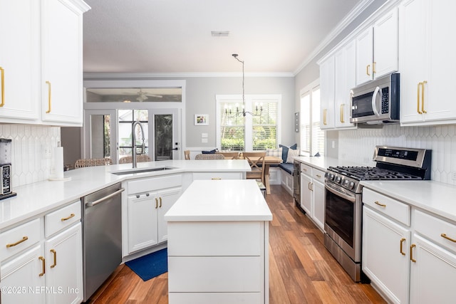 kitchen featuring appliances with stainless steel finishes, ornamental molding, wood finished floors, a peninsula, and a sink