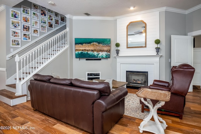 living area with a fireplace, wood finished floors, visible vents, stairs, and ornamental molding