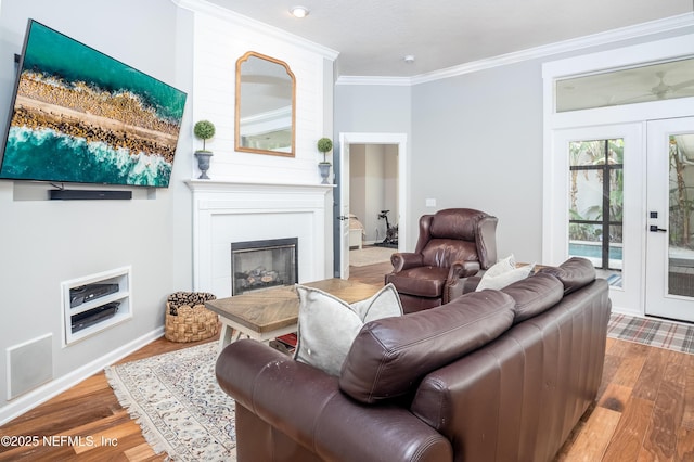 living area with french doors, ornamental molding, a tiled fireplace, and wood finished floors