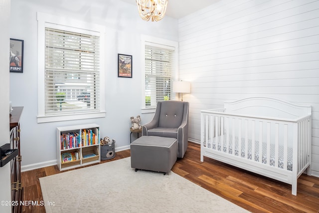 bedroom with a nursery area, baseboards, an inviting chandelier, and wood finished floors