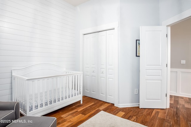 bedroom featuring a closet, a decorative wall, a crib, and wood finished floors