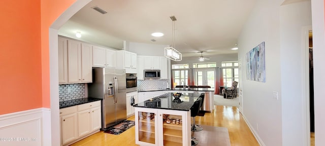 kitchen with a peninsula, visible vents, appliances with stainless steel finishes, light wood-type flooring, and backsplash