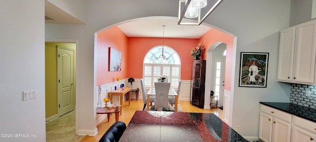 dining area featuring light wood-type flooring, wainscoting, a decorative wall, and arched walkways