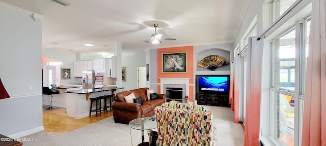 living room with light carpet, baseboards, ceiling fan, crown molding, and a fireplace