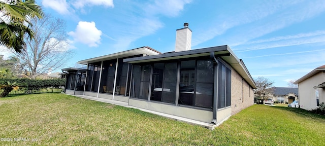 rear view of house featuring a sunroom, a chimney, and a lawn