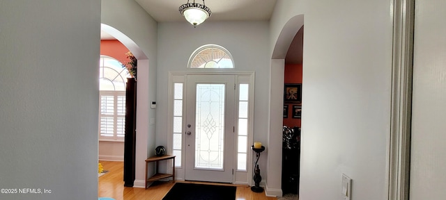 foyer entrance with light wood-style floors, arched walkways, and baseboards