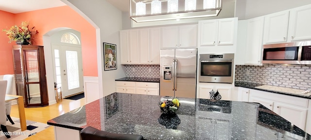 kitchen with arched walkways, tasteful backsplash, appliances with stainless steel finishes, light wood-style floors, and white cabinetry