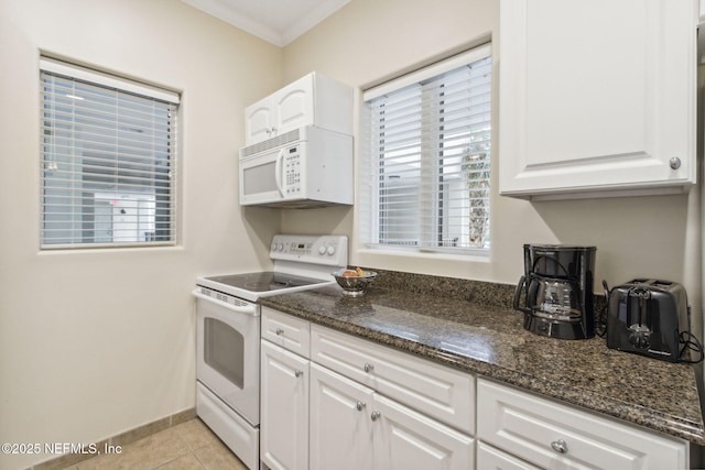 kitchen with light tile patterned floors, ornamental molding, white cabinets, dark stone countertops, and white appliances