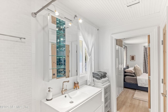 ensuite bathroom featuring visible vents, a shower, ornamental molding, wood finished floors, and vanity