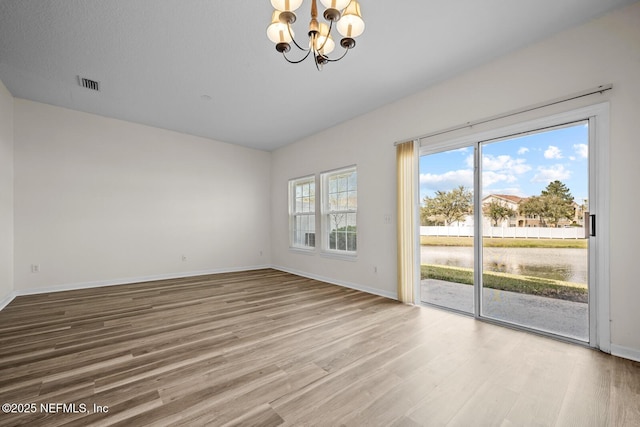 spare room with baseboards, visible vents, a chandelier, and wood finished floors