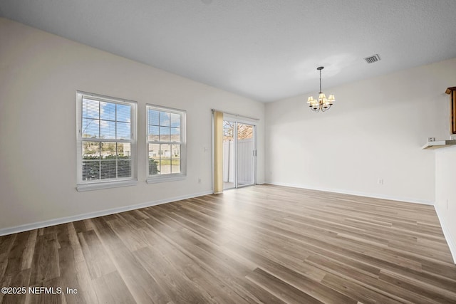 interior space with a chandelier, wood finished floors, visible vents, and baseboards