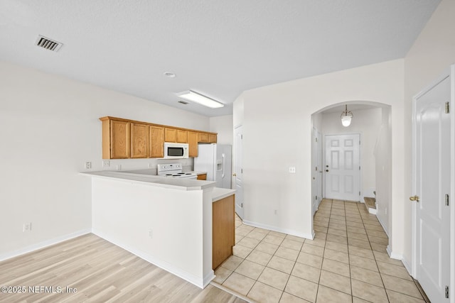 kitchen featuring arched walkways, a peninsula, white appliances, visible vents, and light countertops