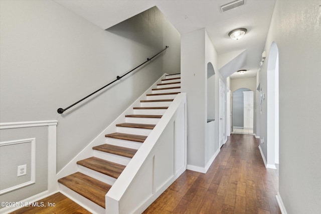 staircase featuring baseboards, visible vents, arched walkways, and hardwood / wood-style floors