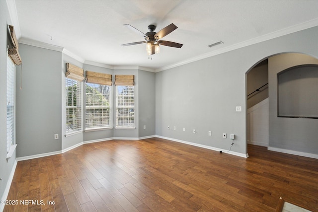 empty room featuring wood finished floors, visible vents, baseboards, a ceiling fan, and ornamental molding