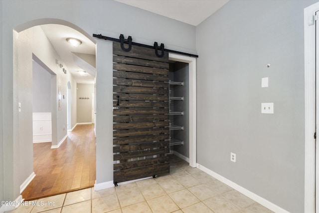 interior space featuring light tile patterned floors, a barn door, built in features, arched walkways, and baseboards