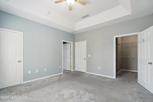 unfurnished bedroom featuring carpet floors, a tray ceiling, visible vents, and baseboards