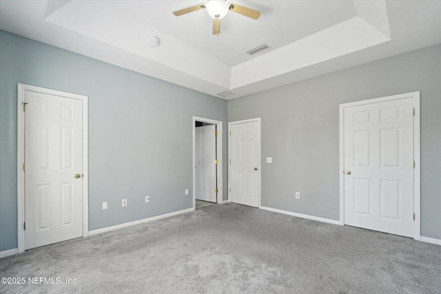 unfurnished bedroom with carpet floors, a tray ceiling, visible vents, and baseboards