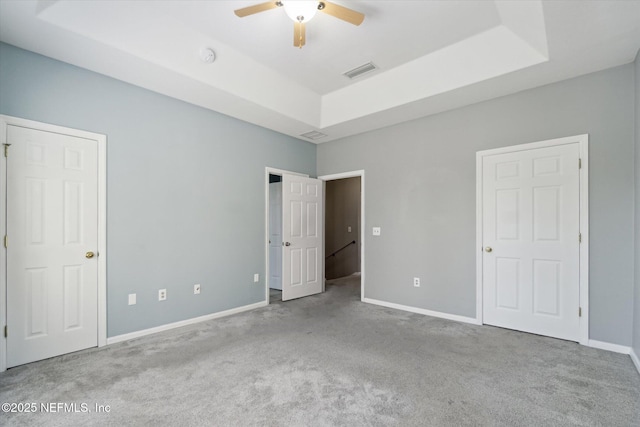 unfurnished bedroom featuring carpet, a raised ceiling, visible vents, and baseboards