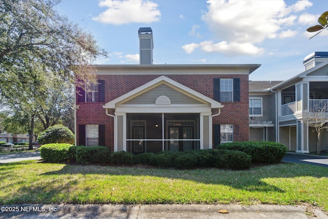 view of front of house featuring a sunroom, brick siding, and a front lawn