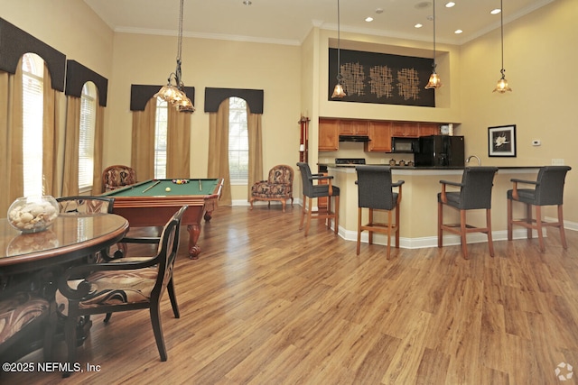 game room with ornamental molding, a towering ceiling, light wood-style flooring, and baseboards