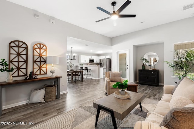 living room with ceiling fan with notable chandelier, wood finished floors, visible vents, and baseboards