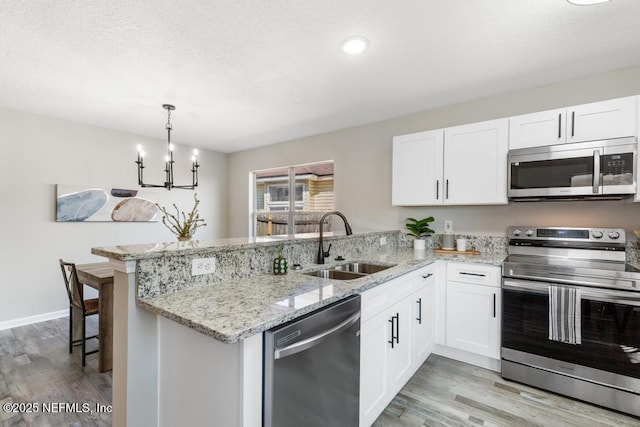 kitchen with light wood-style flooring, stainless steel appliances, a peninsula, a sink, and white cabinetry