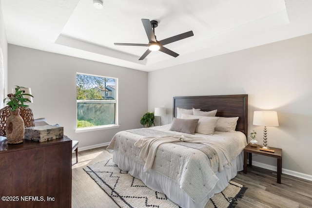 bedroom with ceiling fan, light wood-type flooring, a raised ceiling, and baseboards