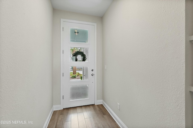 doorway featuring wood finished floors, baseboards, and a textured wall