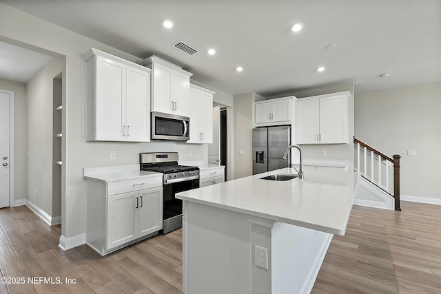 kitchen featuring a sink, light wood-type flooring, appliances with stainless steel finishes, and an island with sink