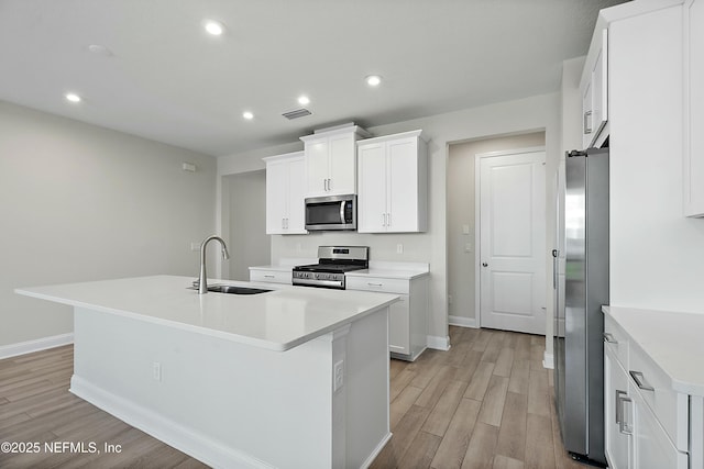 kitchen with an island with sink, a sink, white cabinets, light wood-style floors, and appliances with stainless steel finishes