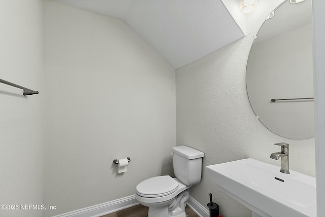 bathroom featuring toilet, a sink, wood finished floors, baseboards, and vaulted ceiling