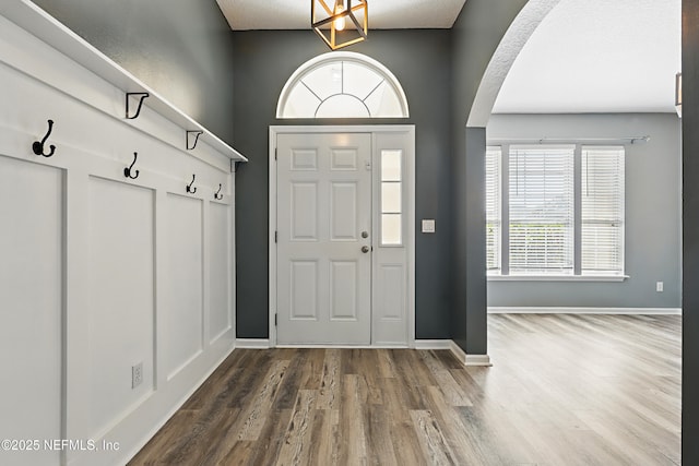 entryway with arched walkways, dark wood-type flooring, and baseboards