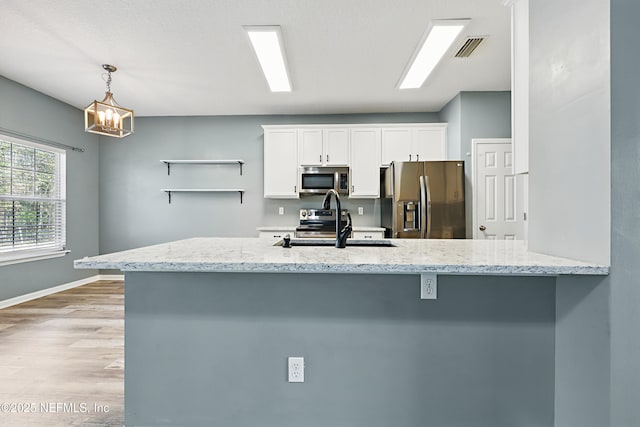 kitchen featuring light stone counters, light wood-style flooring, stainless steel appliances, visible vents, and white cabinets