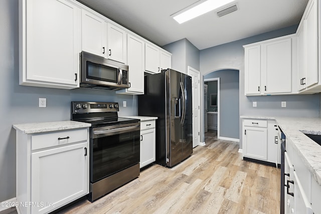 kitchen featuring arched walkways, light stone counters, white cabinetry, light wood-style floors, and appliances with stainless steel finishes