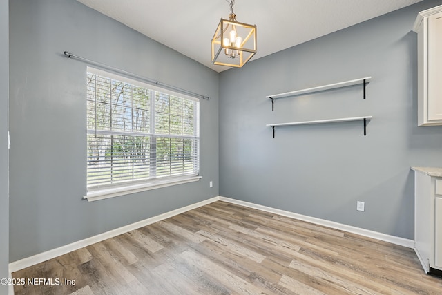 empty room featuring baseboards, a notable chandelier, and light wood finished floors