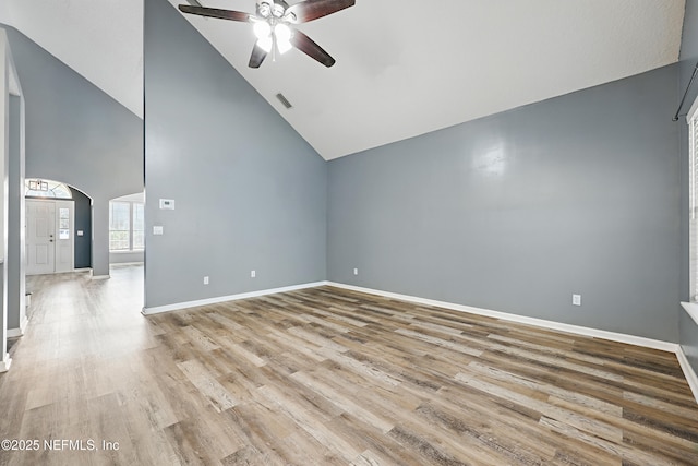 empty room with arched walkways, visible vents, ceiling fan, wood finished floors, and baseboards