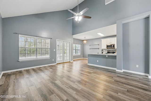 unfurnished living room featuring baseboards, a ceiling fan, wood finished floors, french doors, and high vaulted ceiling