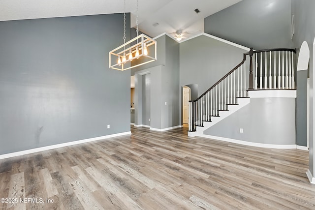 interior space featuring arched walkways, wood finished floors, high vaulted ceiling, baseboards, and stairs