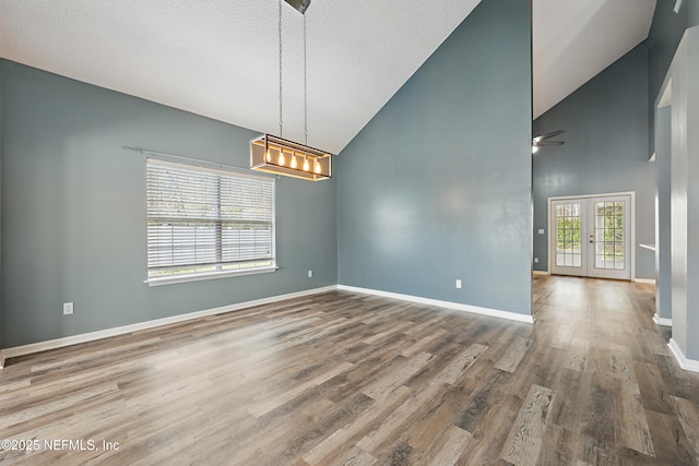 spare room featuring a textured ceiling, high vaulted ceiling, wood finished floors, baseboards, and french doors