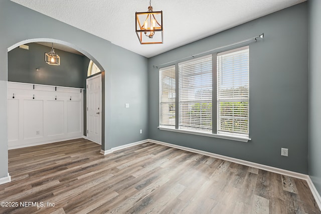 spare room with baseboards, arched walkways, wood finished floors, an inviting chandelier, and a textured ceiling