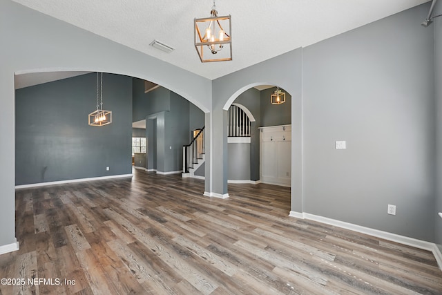 spare room featuring baseboards, lofted ceiling, stairway, wood finished floors, and an inviting chandelier