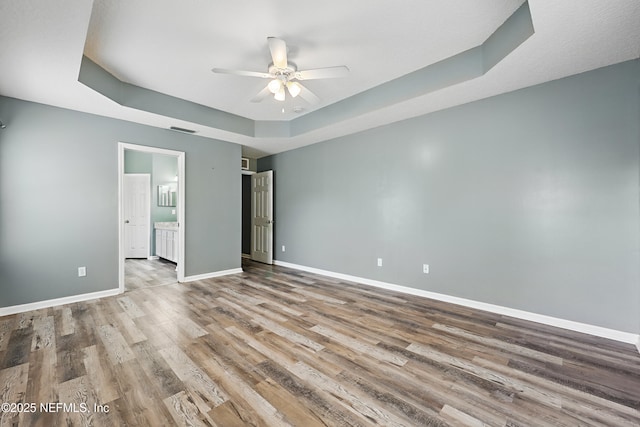 unfurnished bedroom with a raised ceiling, visible vents, ensuite bath, wood finished floors, and baseboards