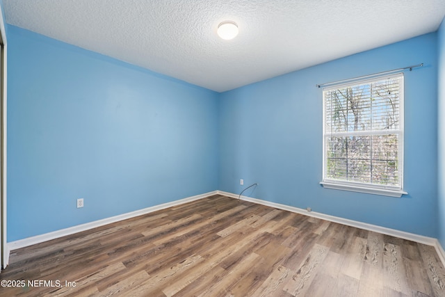 empty room with a textured ceiling, wood finished floors, and baseboards