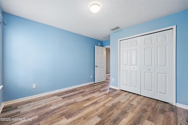 unfurnished bedroom with a closet, visible vents, a textured ceiling, wood finished floors, and baseboards