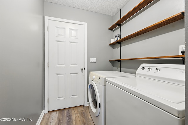 washroom with a textured ceiling, washing machine and dryer, laundry area, wood finished floors, and baseboards