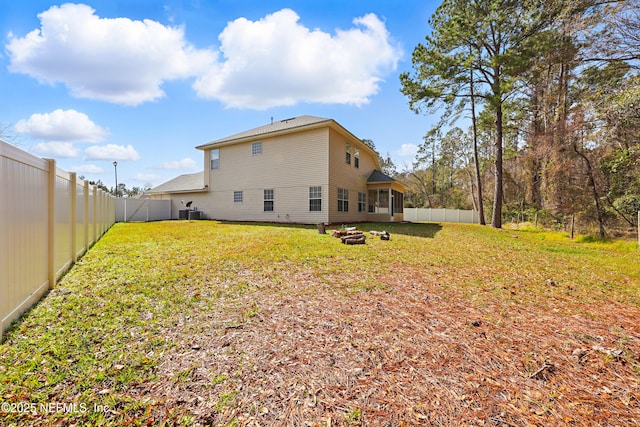 rear view of property featuring a fenced backyard, a fire pit, and a yard