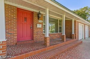 view of exterior entry featuring brick siding and a porch